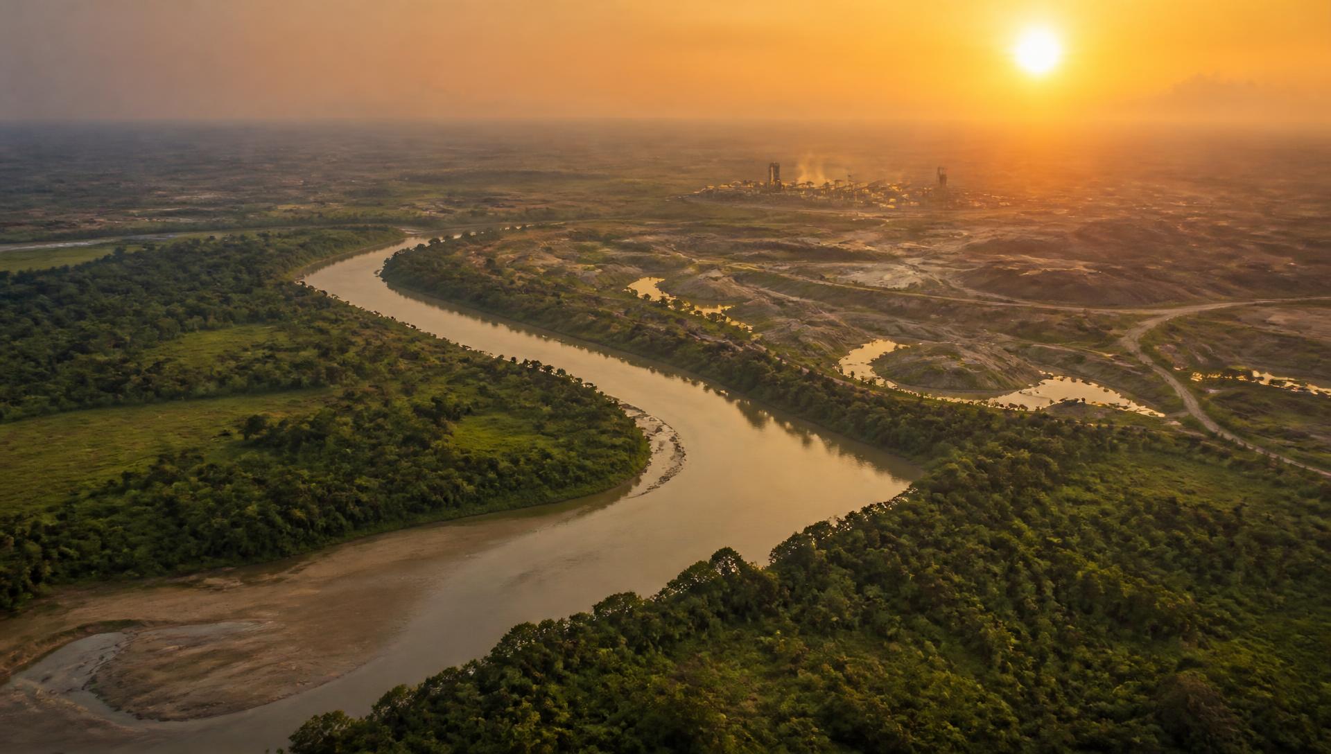 Paysage de savane traversé par un fleuve, avec une installation industrielle à l'horizon